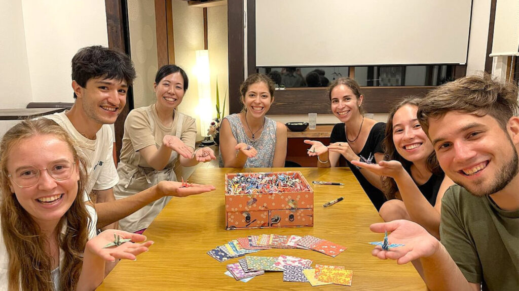 多国籍の宿泊者が折り鶴体験を楽しむ様子。旅人同士が笑顔でつながる。 | Guests from around the world enjoy making origami cranes together – travelers smiling and connecting at Kanazawa Guesthouse Pongyi.