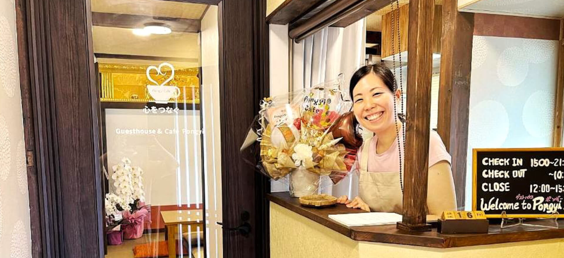 女将が笑顔で迎えるフロント。旅人との温かい交流が生まれる場所。 | The front desk where the hostess of Kanazawa Guesthouse Pongyi welcomes guests with a smile – a warm place where travelers connect
